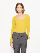 Top de punto acanalado color amarillo, con escote cuadrado y mangas largas. Presenta un corte ajustado al cuerpo y largo hasta la cadera.