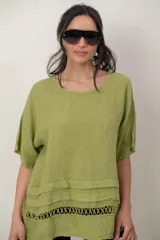 Blusa de lino color blanco, de corte amplio, con escote redondo, mangas cortas y detalle de guarda calada horizontal en la parte inferior.