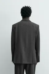 Blazer de corte regular fit en color gris oscuro, confeccionada en tejido con viscosa. Presenta cuello con solapas de muesca, cierre frontal con dos botones, bolsillos laterales con solapa y aberturas en la espalda.