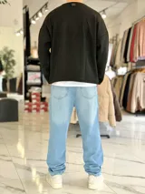 Sweater de punto liviano color beige, con textura marcada, cuello redondo y mangas largas de corte relajado, con pequeño estampado tipográfico negro en el lateral inferior.