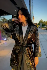 Kimono de terciopelo verde con detalles de lentejuelas en los bordes frontales y en los puños. Presenta un diseño de manga larga amplia, corte holgado y lazo ajustable en la cintura.