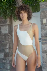 Malla enteriza con diseño asimétrico de bloques de color en blanco y dorado. Presenta un corte cavado y escote redondo.