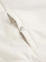 Chaleco blanco hueso acolchado, con cuello alzado de punto de canalé, cierre frontal con cremallera, bolsillos laterales con botón a presión y logo de Calvin Klein en el pecho.