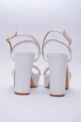 Sandalia de cuero con plataforma y taco cuadrado alto. Presenta una tira delgada en el tobillo con cierre de hebilla metálica y dos tiras acolchadas en la parte frontal.