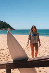 Remerón cropped color hueso con estampado frontal de tres cuadrados azules que contienen un hibisco, una ola y una concha marina, y la frase "Glassy Waves".