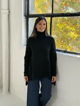Sweater de punto color negro con cuello alto tipo polera, diseño holgado y corte asimétrico con la parte trasera más larga.