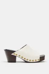 Zueco de piel color blanco, con tacón de madera y plataforma, detalle de tachas metálicas doradas en los laterales y punta cuadrada.