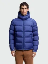 Campera puffer Moncler modelo Maya, color azul, con capucha integrada, cierre frontal bidireccional y bolsillo con solapa en la manga izquierda.