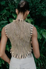 Top sin mangas de cuello redondo con lazo frontal, confeccionado en tejido con textura de nido de abeja elástico y estampado de rayas verticales. Presenta terminaciones con volantes en el ruedo.