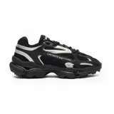 Championes Lacoste modelo L003 2K24, de diseño deportivo y urbano. Presentan una combinación de malla y superposiciones sintéticas en color negro con detalles reflectantes plateados. Cuentan con una suela robusta y texturizada, y el logo de la marca estampado en el lateral.