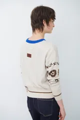 Buzo de tejido de punto en color beige con estampado de motivos florales y abstractos en tonos marrones. Presenta cuello redondo con borde en color azul vibrante, mangas largas y puños ajustados.