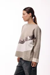 Sweater de punto con diseño de bloques de color en diagonal, combinando negro, beige y una franja central con textura metalizada. Presenta cuello redondo, mangas largas con puños en contraste y un corte holgado.