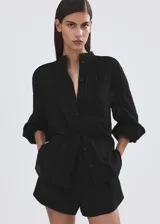 Blusa Lucy de diseño recto color negro, confeccionada en mezcla de algodón y viscosa. Cuenta con cuello mao, detalles bordados calados, manga larga y cierre frontal con botones.