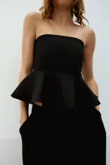 Top negro strapless con escote recto y bajo acabado en peplum. Cuenta con cierre lateral con cremallera oculta en costura.