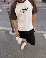 Remera de corte oversize con mangas tipo raglán en color marrón y cuerpo en color blanco. Presenta un estampado central de un auto estilo caricatura en color negro.