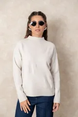 Buzo de punto color visón con cuello alto, manga larga y diseño holgado. Presenta un bordado floral en relieve al tono en la parte frontal.