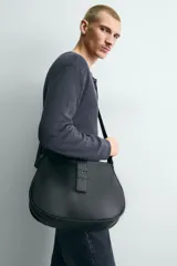 Bandolera negra de cuero sintético con correa ajustable para el hombro y cierre con solapa con hebilla decorativa.