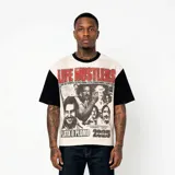 Remera de corte oversize con panel frontal en color beige y mangas y cuello en color negro. Presenta un estampado gráfico central con temática de Pablo Escobar, incluyendo el texto 'Life Hustlers' en rojo, la frase 'El que no conoce su historia está condenado a repetirla', 'Plata o Plomo' y '2025'.