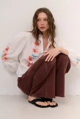 Camisa blanca de manga larga abullonada, con delicados bordados florales en tonos azules y verdes a lo largo de la botonadura frontal y en las mangas. Presenta cuello mao con reborde en contraste y cierre frontal con botones.