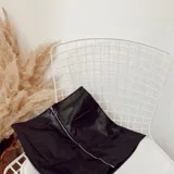Minifalda negra de ecocuero con cierre metálico frontal y dos bolsillos delanteros.