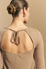 Top negro de manga larga acampanada con escote pronunciado en la espalda que se ajusta con lazos. La tela presenta una textura sutil con brillo, similar a un animal print discreto.