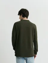 Remera de manga larga con cuello polo, confeccionada en tejido de punto canalé francés. Presenta abotonadura frontal con botones de madera y detalles a contratono en la cartera y el interior del cuello.