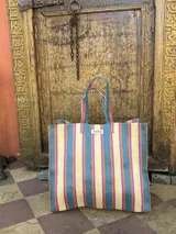 Bolso tipo tote grande con estampado a rayas verticales en tonos celeste, blanco y bordó. Tiene doble asa corta de mano y cierre superior.
