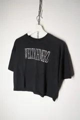 Remera negra de corte cropped con estampa frontal en color blanco que presenta la palabra Weltschmerz con un diseño tipográfico distorsionado.