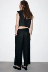 Pantalón negro de tiro medio con pierna ancha y cierre frontal de cremallera con dos botones dorados decorativos.