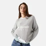 Sweater de tejido de punto, color gris claro, con cuello redondo y manga larga. Presenta un estampado frontal con el texto "EME STUDIOS" y un texto más pequeño debajo.