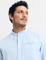 Camisa de cuello mao y manga larga, confeccionada en una mezcla de lino y algodón. Presenta un diseño de corte recto con botones en tono natural y un bolsillo pequeño en el pecho.