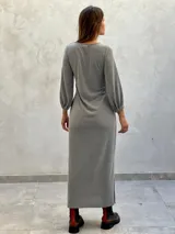 Vestido largo color verde militar, con cuello redondo, mangas largas abullonadas con puños elásticos y detalle de lazo anudado en la cintura. Presenta una abertura lateral en la falda.