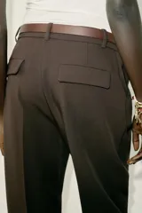 Pantalón tobillero de tiro medio, color beige, con pinzas delanteras y bolsillos frontales. Incluye un cinturón fino de cuero marrón con hebilla metálica dorada y cierre frontal con cremallera, botón interior y gancho.