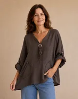 Blusa marrón chocolate de corte amplio, con escote en V, cordones decorativos con apliques de botones de madera, bolsillos frontales de parche y mangas tres cuartos con presilla.