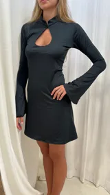 Vestido corto de lycra color negro, con cuello mao, abertura frontal tipo gota y mangas largas acampanadas.