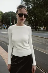 Jersey de punto liso con cuello redondo y manga larga. Presenta detalle de botones decorativos en los puños.