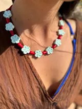 Collar corto con cuentas de flor de cerámica color celeste y cuentas rojas reconstituidas. Se cierra con cadena de acero quirúrgico y ganchito para regular el largo.