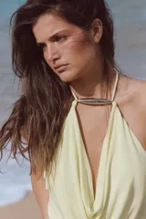 Vestido largo de punto color amarillo claro, con escote fluido tipo cowl, tirantes finos ajustables al cuello y detalle de aplicación metálica en la parte delantera.