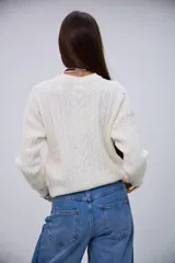 Sweater de punto color crudo con cuello redondo, diseño de ochos y mangas largas.