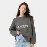 Suéter de punto grueso color gris oscuro, con corte cuadrado y ligeramente corto. Presenta cuello redondo, puños ajustados y el logo de la marca Eme Studios junto a la frase 'curated by ben ice' en jacquard blanco en el frente.