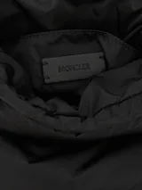 Cartera tipo bucket Moncler modelo Caradoc, de diseño acolchado y color negro, con cierre superior fruncido mediante cordón ajustable, asa superior de hombro y detalle del logo metálico de la marca en el frente.