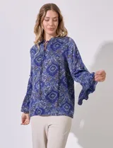 Blusa de satén estampado con motivos arabescos en tonos azules, marca Grand & Greene. Cuello a la base fruncido, escote en V y lazo. Manga larga amplia con terminación acampanada.