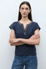 Remera blanca de algodón con escote en V y detalles de bordado étnico en tonos rojizos y naranjas en el cuello y los hombros. De corte recto y manga corta.