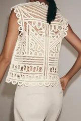 Blusa sin mangas confeccionada en tejido tipo crochet con diseño geométrico calado, cuello redondo y cierre frontal con botones.