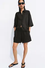 Shorts de tiro medio confeccionados en 100% lino, de color negro. Presentan cintura elástica con volado y cordón ajustable, además de bolsillos delanteros aplicados.