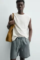 Bermuda de lino color blanco hueso, de corte relajado y tiro medio. Presenta cintura elástica ajustable con cordón, pliegues frontales y bolsillos laterales y trasero.