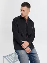 Sobrecamisa de manga larga confeccionada en pana de algodón, con cuello camisero, cierre frontal de botones, puños abotonados y un bolsillo en el pecho. Presenta un corte relajado y textura acanalada.