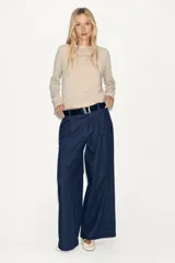 Jersey de punto color beige claro, manga larga y cuello redondo. Presenta un detalle de tejido a contraste (posiblemente una tela blanca con estampado sutil) asomando en el ruedo y el cuello.