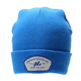 Gorro tipo beanie de tejido de punto color azul, con vuelta y parche frontal rectangular con bordes redondeados que incluye logo y texto impreso.