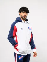 Campera deportiva Umbro del Club Nacional de Football, con cierre frontal, capucha ajustable con cordones y diseño en bloques de color azul, celeste y blanco. Presenta el logo de la marca y el escudo del club bordados en el pecho.